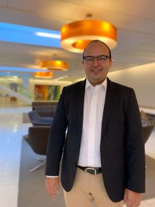 Es una foto de medio cuerpo del doctor Edwin Nemesio Álvarez. En la imagen se encuentra vestido con una camisa oxford blanca, un blazer azul marino oscuro y pantalones color beige.